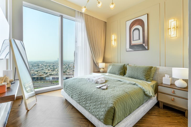 Sage-green bedroom with floor-to-ceiling windows overlooking the city.